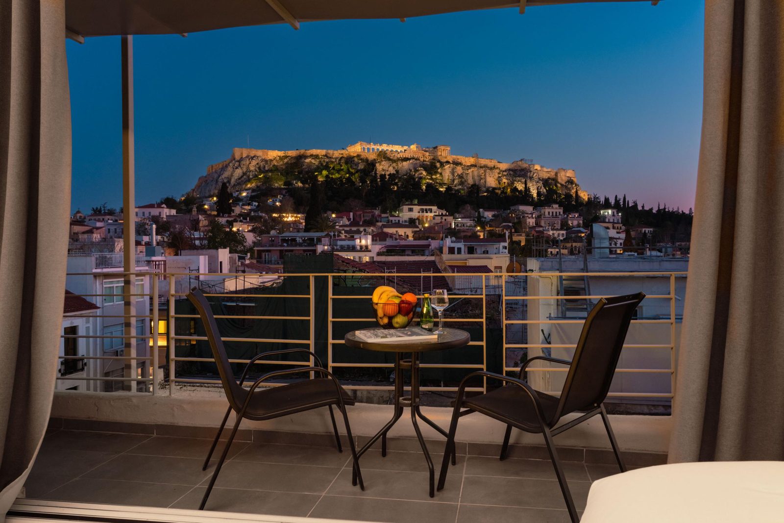 The Acropolis lit at dusk, seen from a terrace with two chairs at 24K Athena Suites